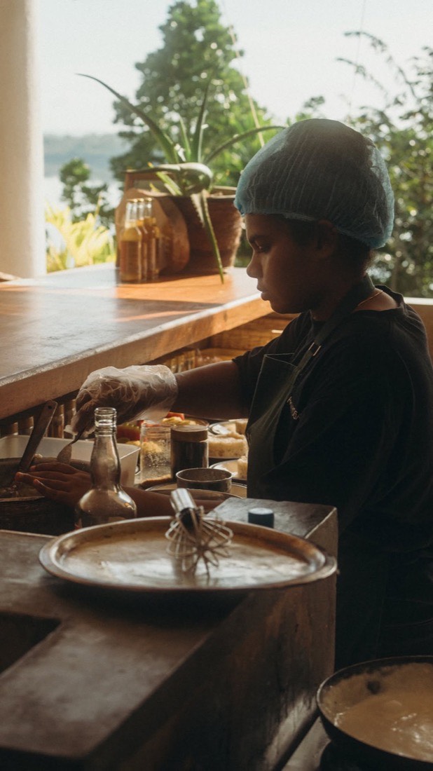 A cook preparing plant-based food in the open-air lakeside kitchen at Lanka Yoga